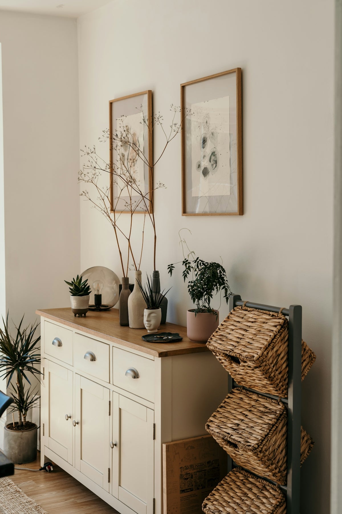 A wooden sideboard with potted plants, vases, and wicker baskets in a living room